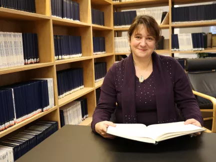 Student smiling in library reading book